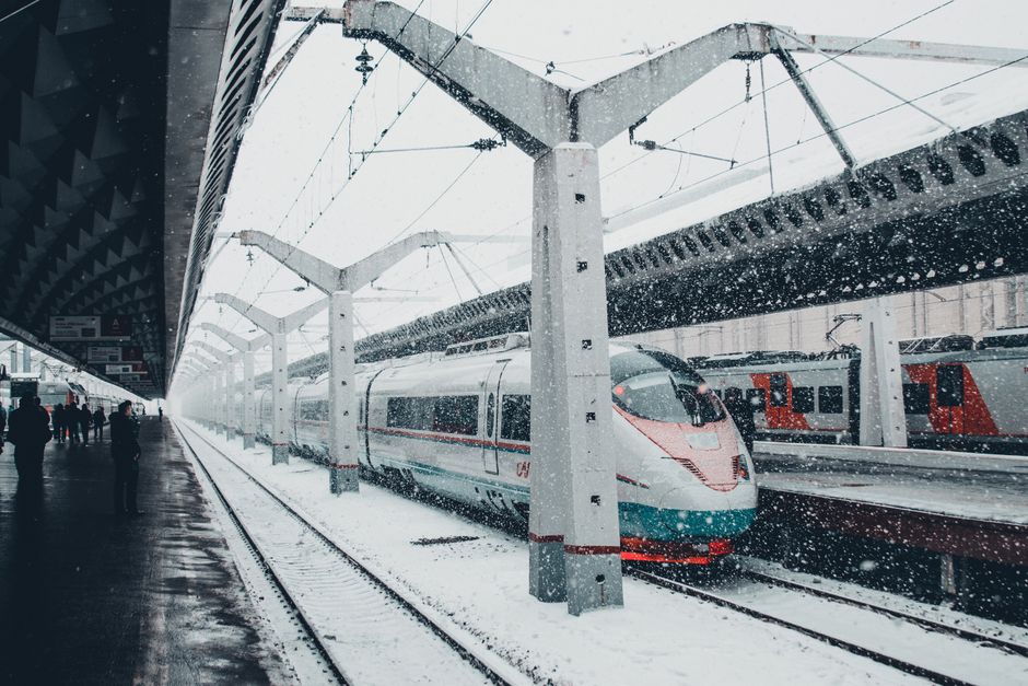 A sleek high-speed train at a snow-covered urban station during winter snowfall.
